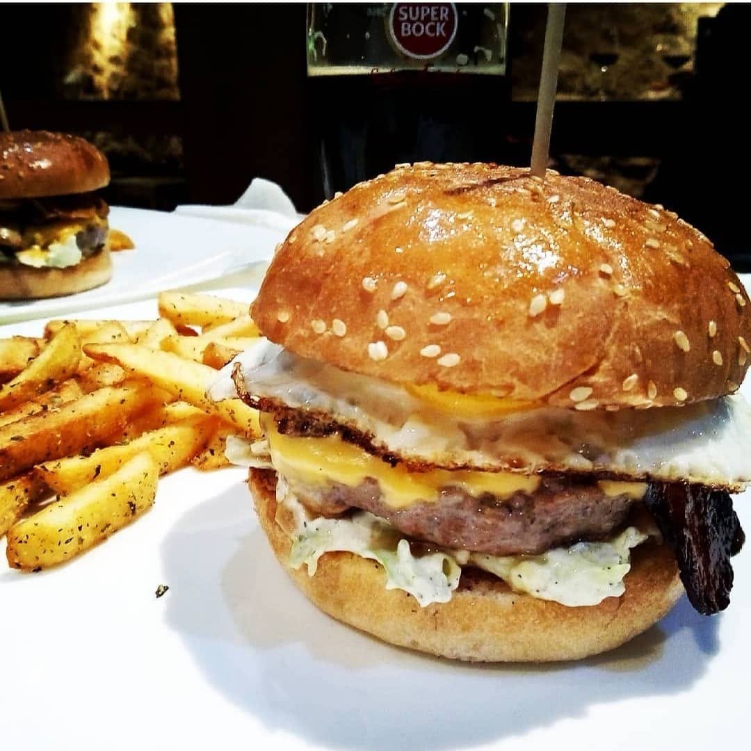 Hambúrguer em pão com sésamo, com ovo estrelado e queijo, e batatas fritas